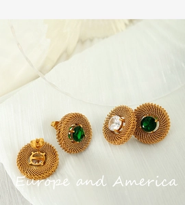 Detail view of vintage gold mesh earrings with green and clear gemstones on white fabric