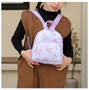 Toddler girl wearing a purple cartoon bear backpack with ears on a home background