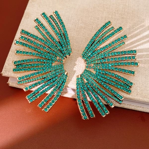Detailed view of fan-shaped gold earrings with turquoise rhinestones on book surface
