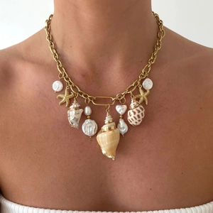 Detail of gold titanium necklace with seashells, starfish and baroque pearls on skin