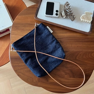 Detail of navy denim crossbody bag with simple wish label and leather strap on wooden table