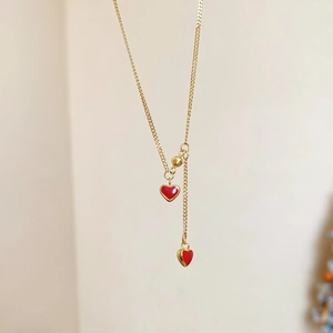 Macro detail of golden Y-chain necklace featuring dual red enamel heart pendants