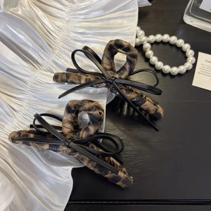 Close-up of leopard print fabric hair claw clip with black leather bow and pearl accents