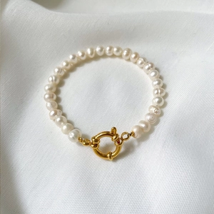 Elegant baroque pearl bracelet with gold OT clasp on a white textured fabric background