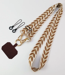 Close-up of leaf pattern woven phone strap with gold hardware and pearl pendant