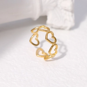 Detail of gold-plated hollow heart-linked open ring on white textured surface