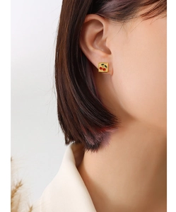 Gros plan de boucles d'oreilles carrées dorées à motif cerise portées par un modèle