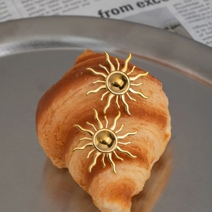 Elegant sun-shaped 18K gold plated stainless steel stud earrings on a rustic french tray