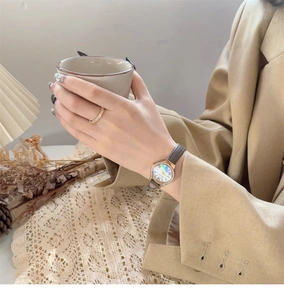 Elegant women's watch with shell dial and gold ring in a warm lifestyle setting