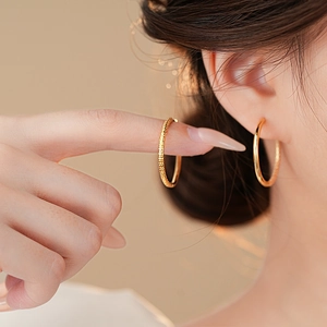 Elegant gold plated textured hoop earrings for women worn by a model in a luxury setting