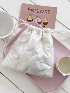 Detail of cream quilted drawstring pouch with embossed bow pattern for cosmetics
