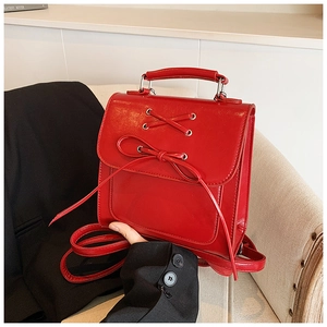 Detailed view of red glossy PU leather backpack with decorative bows and ribbon straps