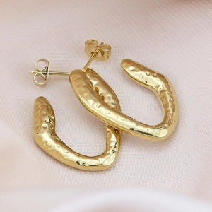 Macro detail of gold U-shaped hoop earrings with irregular hammered texture on silk