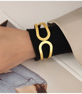 Detail of a minimalist gold geometric open bangle worn over a black knitted sleeve