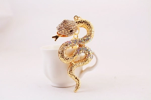 Close-up of a golden snake keychain with colorful rhinestones coiled on a white tea cup
