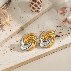 Detail of gold and silver knot earrings on textured stone with pearls and shells
