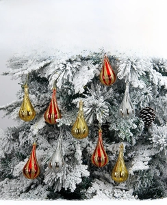 Detail of teardrop Christmas ornaments with glitter stripes on a snowy tree branch