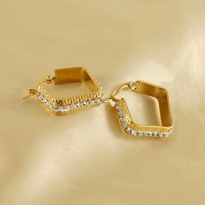 Detail view of gold square earrings with white zircons and Greek key pattern on silk