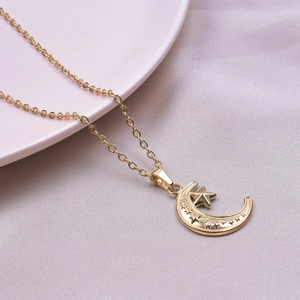 Detail of 18k gold plated moon and star pendant necklace on a pink ceramic plate