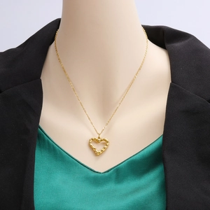Detail of a hollow gold heart pendant necklace on a model with a textured metal finish