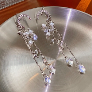 Detail of silver long tassel earrings with diamond moon, stars and white pearls on metal tray