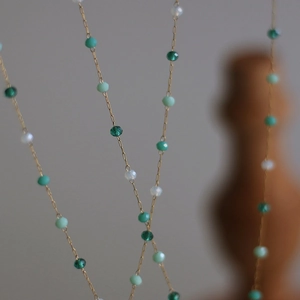 Macro detail of fine gold chain necklace with emerald green and pearl facet beads
