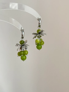 Detail of silver flower earrings with green crystal grape tassel on clear display