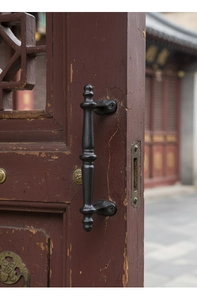 Macro detail of retro black iron door handle installed on vintage dark red wood door