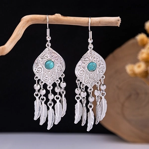 Close-up of bohemian turquoise earrings with metallic feather tassels on a wooden branch