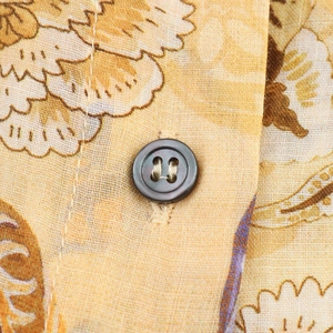 Vista macro del tessuto in misto lino con stampa floreale e dettaglio bottone grigio scuro