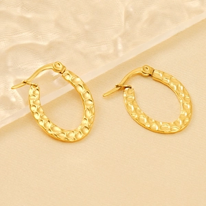 Gold plated oval hammered texture stainless steel earrings on beige silk background