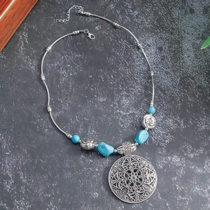 Detail of bohemian silver necklace with turquoise beads and large floral cutout pendant