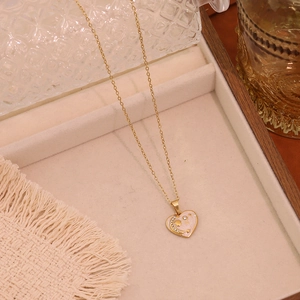 Detail of gold heart pendant necklace with moon and star patterns and white enamel