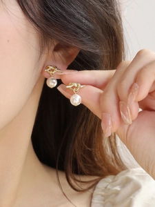 Close-up of elegant gold knotted earrings with white pearls worn by a model