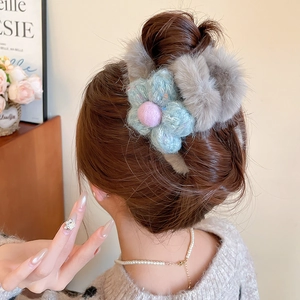 Detail of grey faux fur claw clip with a blue knitted flower worn on a model's hair