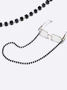 Detail of gold eyewear chain featuring black square crystal beads on a white background
