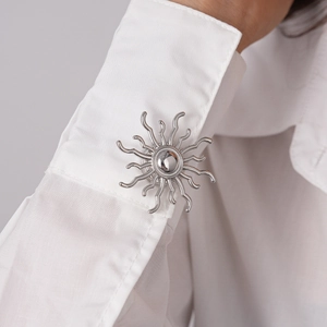 Detail of silver sunburst brooch and cufflink set on white shirt sleeve for formal wear