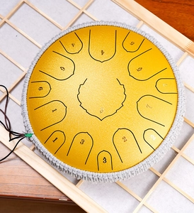 Top view of a gold steel tongue drum with braided rope edge on a wooden grid stand