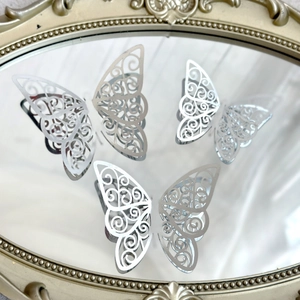 Three silver hollow butterfly cake toppers displayed on a decorative gold-rimmed mirror