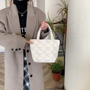 Detail of white quilted tote bag with rabbit patterns shown in a lifestyle indoor setting