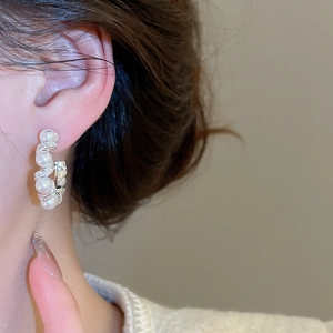 Detailed macro view of C-shaped pearl earrings with cubic zirconia on model ear