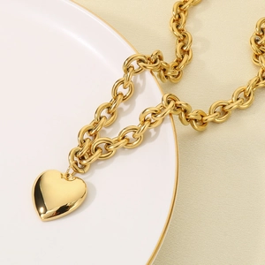 Détail d'un collier avec pendentif cœur en acier inoxydable doré sur une assiette blanche