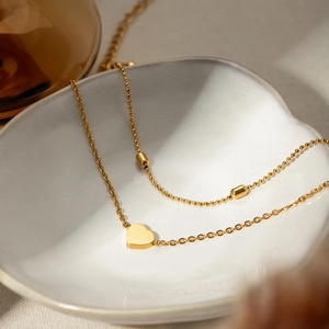 Detail view of a double-layered 18K gold snake chain with heart pendant and small beads