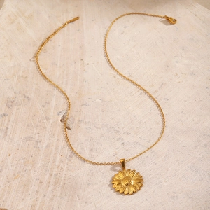 18K gold plated stainless steel sunflower pendant necklace on a beige textured stone