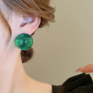 Gros plan d'une boucle d'oreille sphérique verte en résine portée par un mannequin