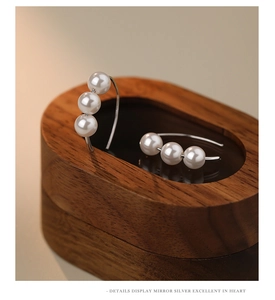 Close-up of triple pearl silver drop earrings resting on a walnut jewelry box edge