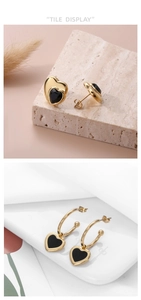 Detail of C-shaped heart earrings in gold finish with black enamel inlays on white background