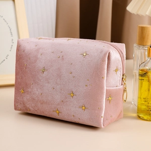 Pink velvet cosmetic bag with gold star patterns and makeup accessories on a desk