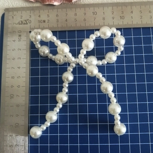 Close-up of white faux pearl bow accessory with scale ruler showing 10x11cm size
