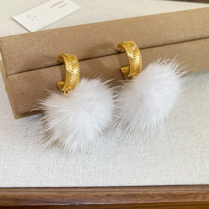 Detail of flower stud earrings featuring white pom-pom drops and textured gold hooks